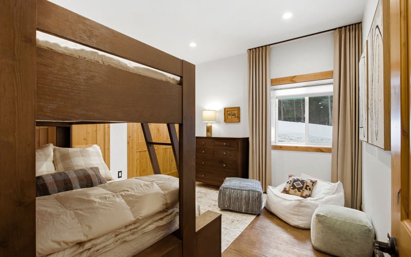 A wooden bunk bed, a wooden dresser, and lounge seating in a bright bedroom with floor-to-ceiling curtains.