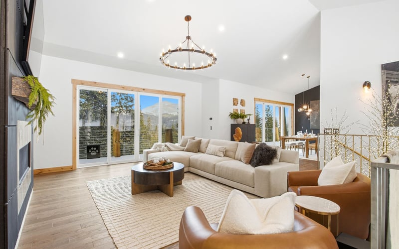 A spacious, modern living room with a cream sectional sofa, two leather armchairs, a rug, and large glass sliding doors.