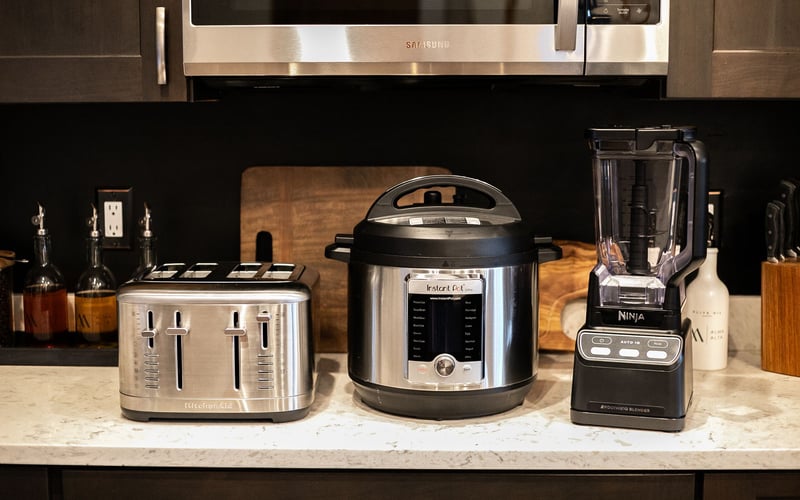 A stainless steel toaster, an Instant Pot, and a black blender sit on a kitchen counter beneath a microwave.