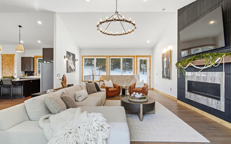 A modern living room with a gray sectional, two leather chairs, a coffee table, fireplace, and open-plan kitchen.