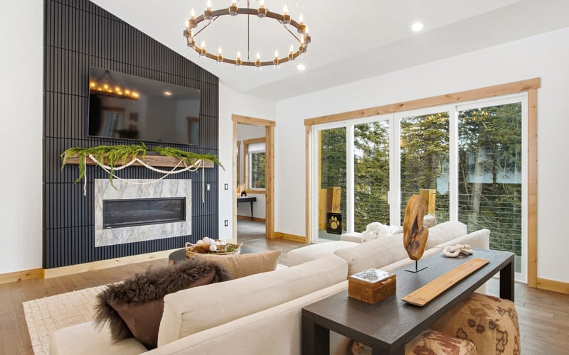 A modern living room with a fireplace, a mounted TV on a dark slat wall, a white sofa, and large sliding glass doors.