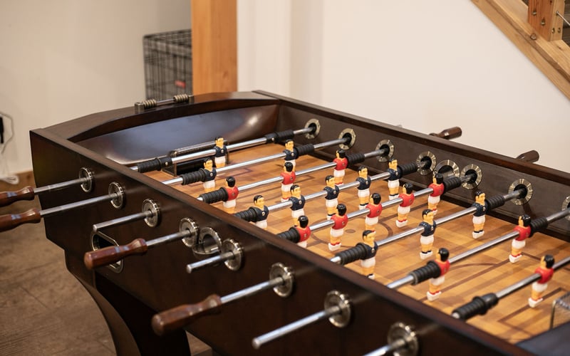 A wooden foosball table with red and black player figurines set on metal rods in a room with light-colored walls.